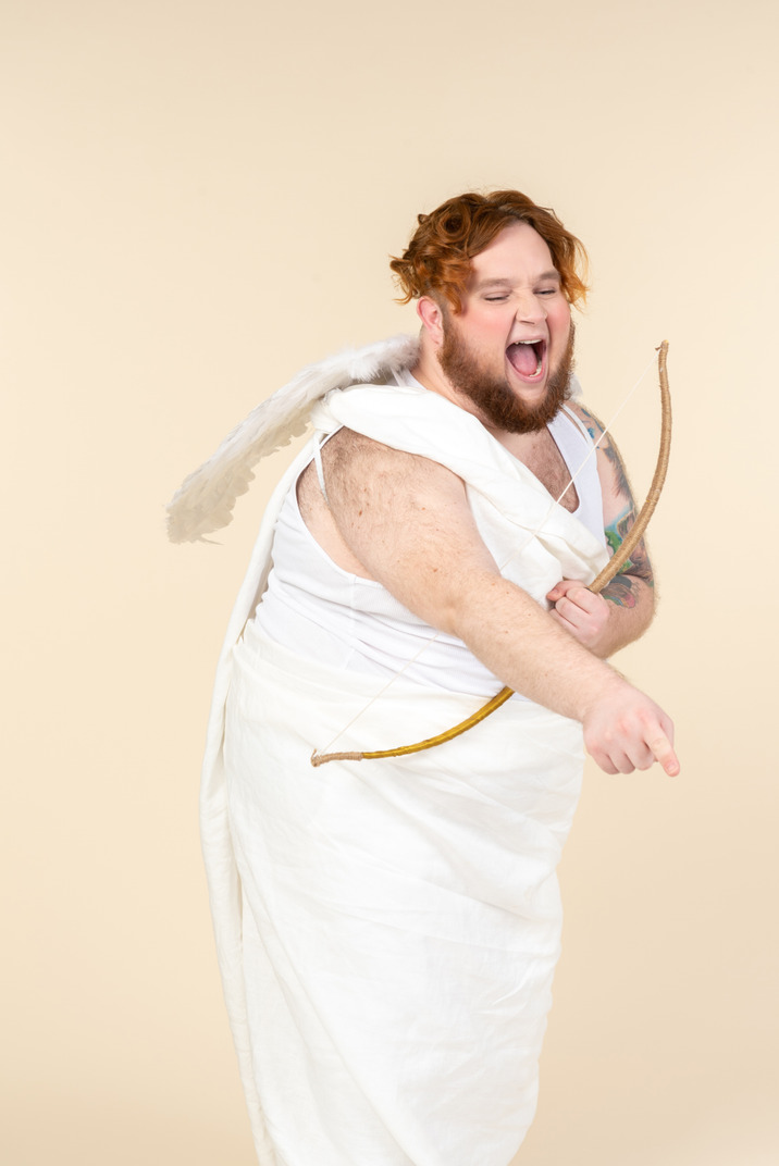 Laughing big guy dressed as a cupid holding bow and arrow and pointing forward