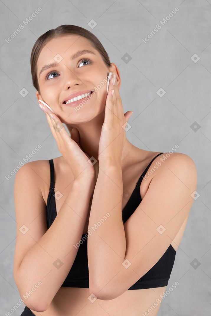 Smiling young woman removing makeup with cotton pads