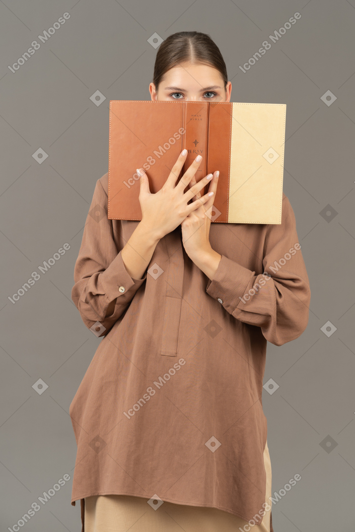 Mujer cubriendo la cara con un libro y mirando a la cámara