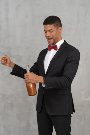 Cheerful man pulling a cork out of a bottle