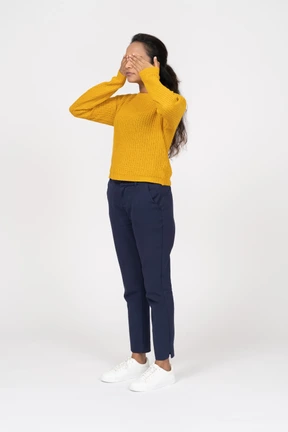Front view of a girl in casual clothes covering eyes with hands