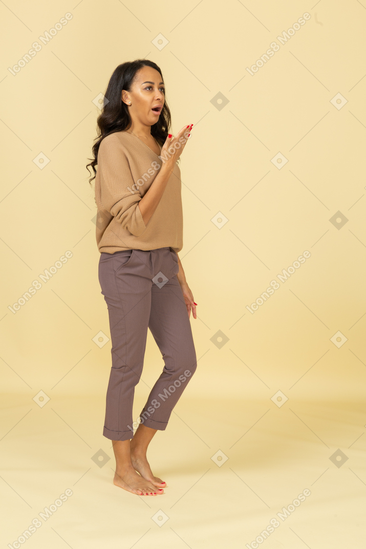 Three-quarter view of a talking young dark-skinned female raising her hand