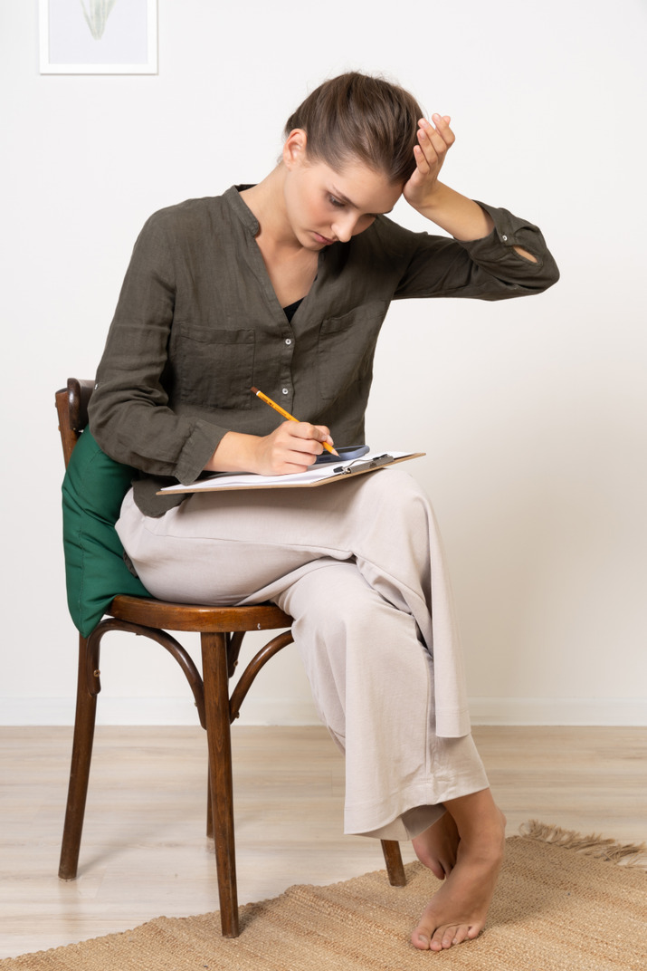 Front view of a thoughtful young woman sitting on a chair while passing paper test