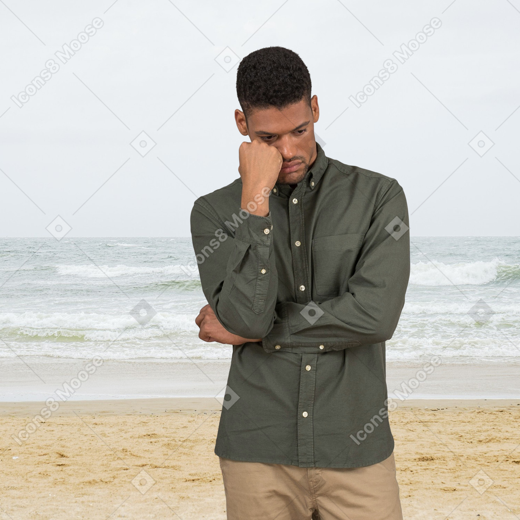 A man standing on a beach with his hand to his face
