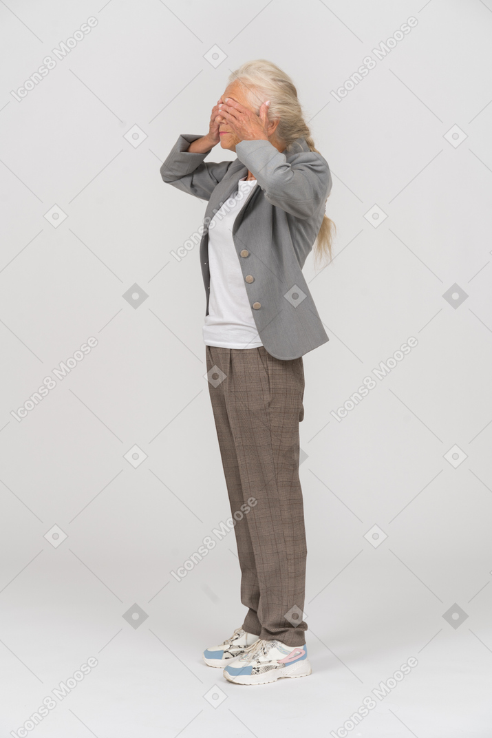 Side view of an old lady in suit covering eyes with hands