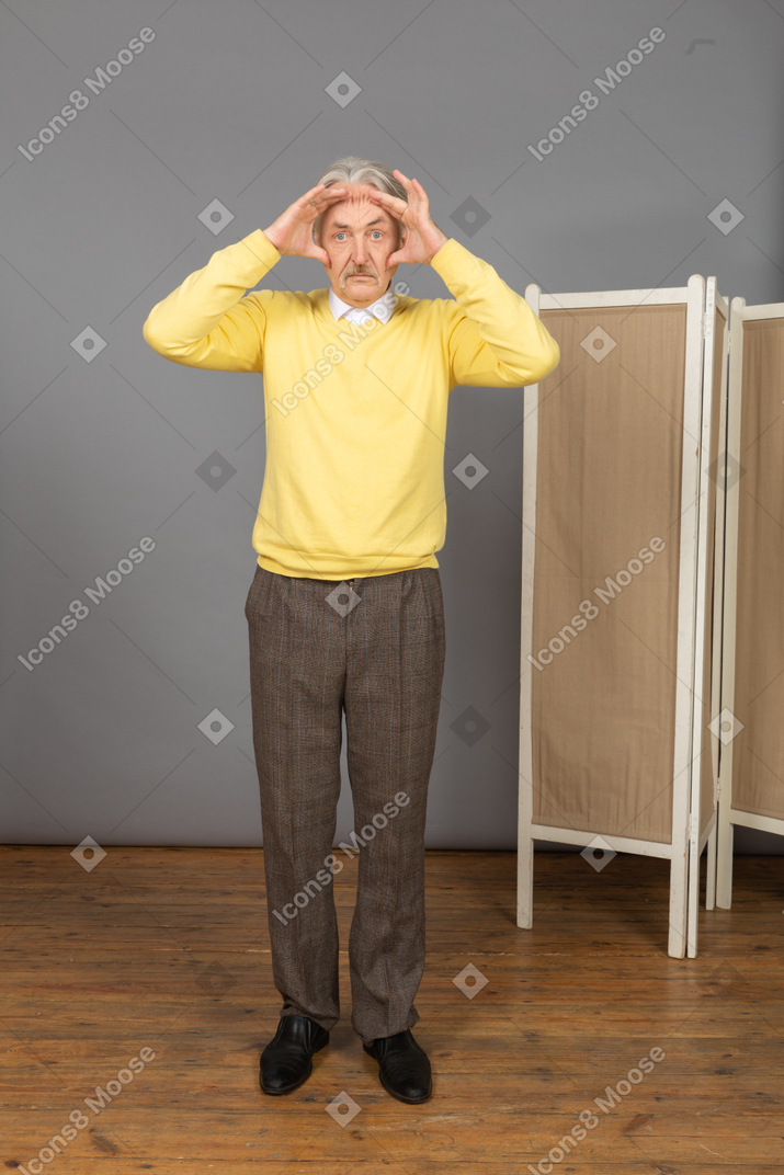Vista frontal de un anciano tocando su cabeza mientras mira a la cámara