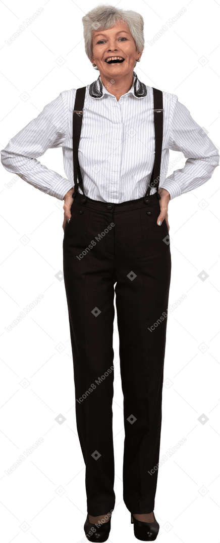 A smiling old woman dressed in trousers and suspenders smiling and putting hands in hips