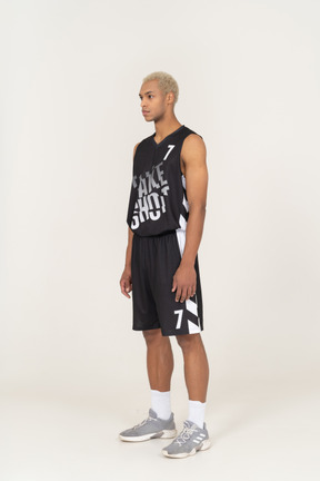 Vista di tre quarti di un giovane giocatore di basket maschile in piedi immobile e guardando da parte