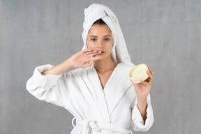 Femme en peignoir avec de la crème pour les mains sur son doigt