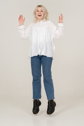 Vista frontale di una giovane donna sorpresa in abiti casual, saltando e alzando le mani