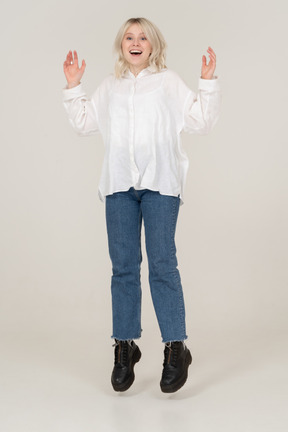 Front view of a surprised young female in casual clothes jumping and raising hands