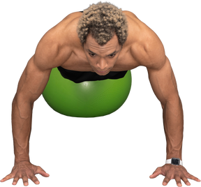 Vista frontal de um homem afro sem camisa fazendo flexões em uma bola de ginástica