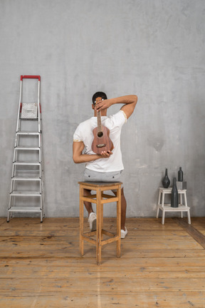 Back view of a man on a stool holding an ukulele behind his back