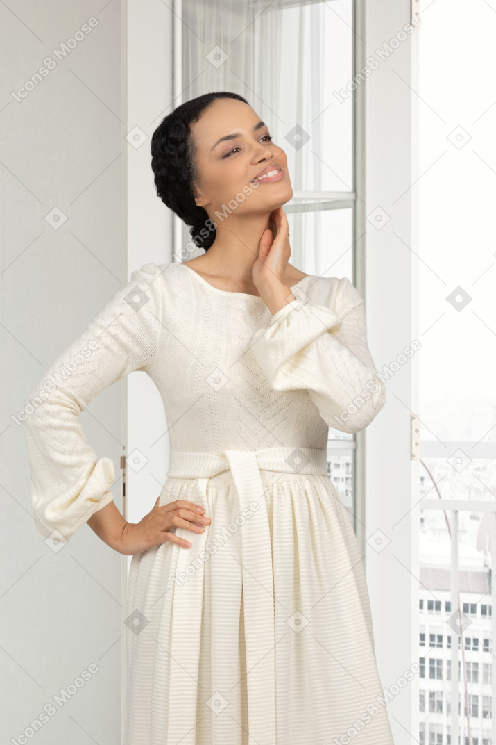 A woman standing in front of a window wearing a white dress