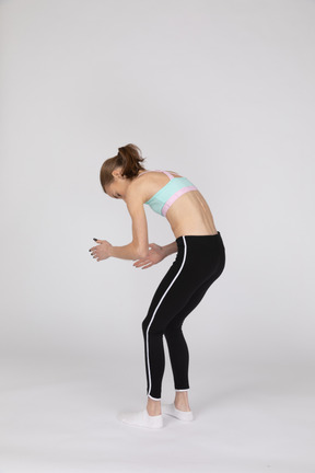 Three-quarter back view of a teen girl in sportswear bending over and raising her hands