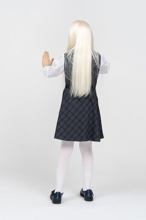Back view of a schoolgirl with both hands up