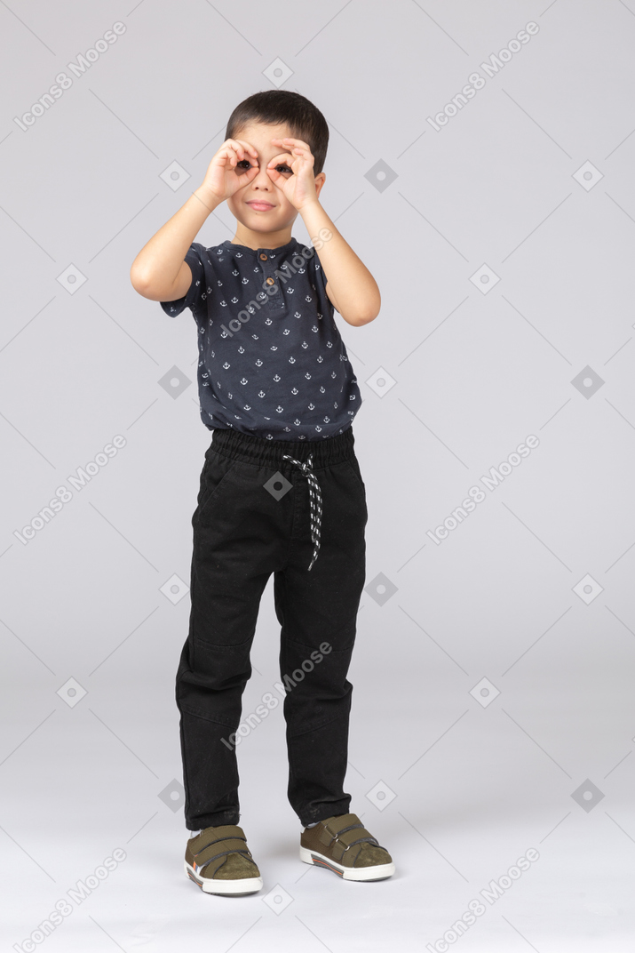 Vista frontal de um menino bonito em roupas casuais olhando por entre os dedos
