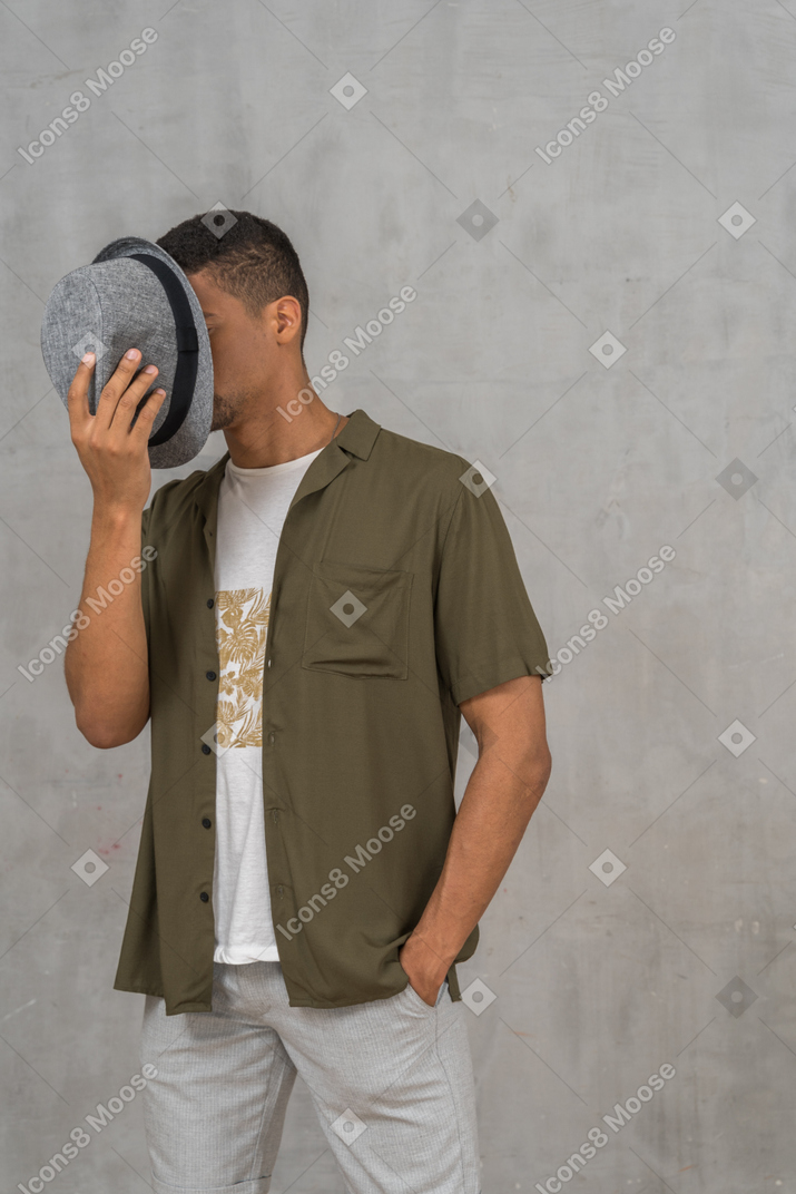 Hombre con ropa informal cubriéndose la cara con un sombrero