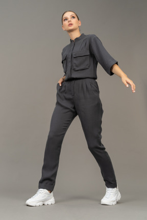 Three-quarter view of a walking young woman in a jumpsuit holding hand in pocket