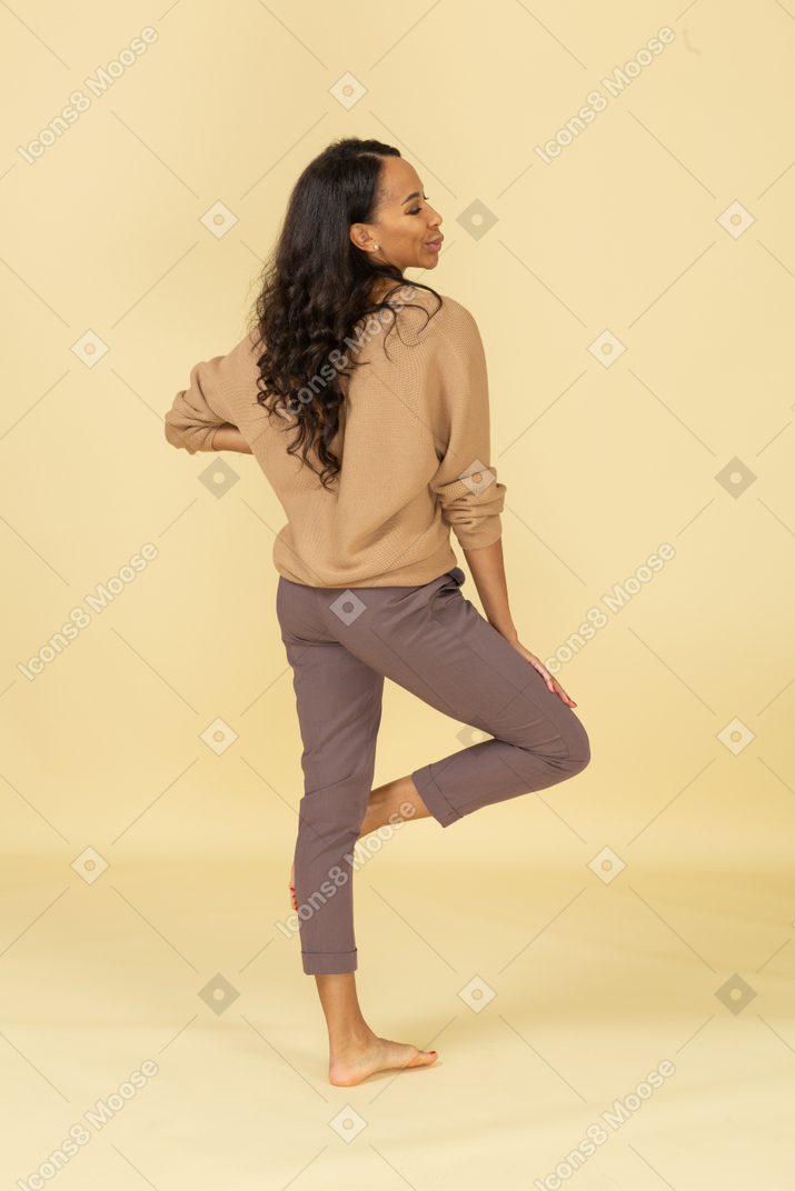 Three-quarter back view of a  grimacing young dark-skinned female putting hand on hip