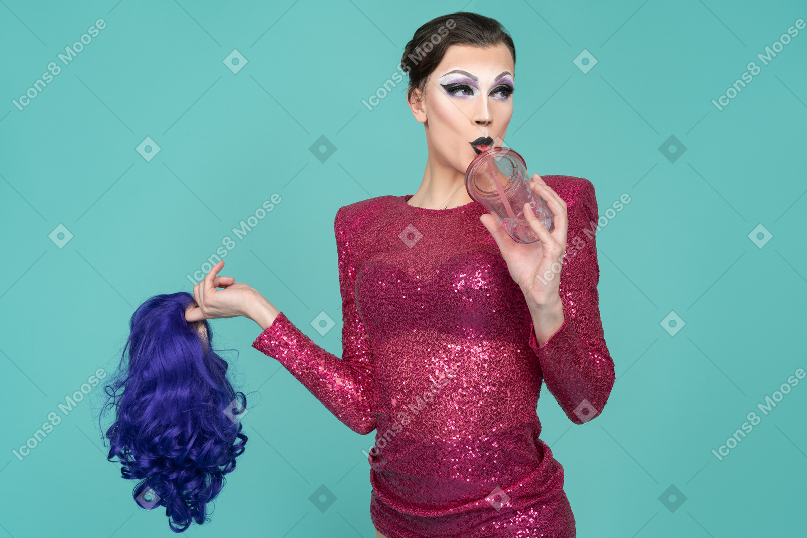 Gros plan d'une drag queen en robe rose buvant à travers de la paille et tenant une perruque