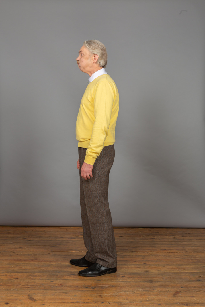 Side view of an old pouting man in yellow pullover looking aside and grimacing