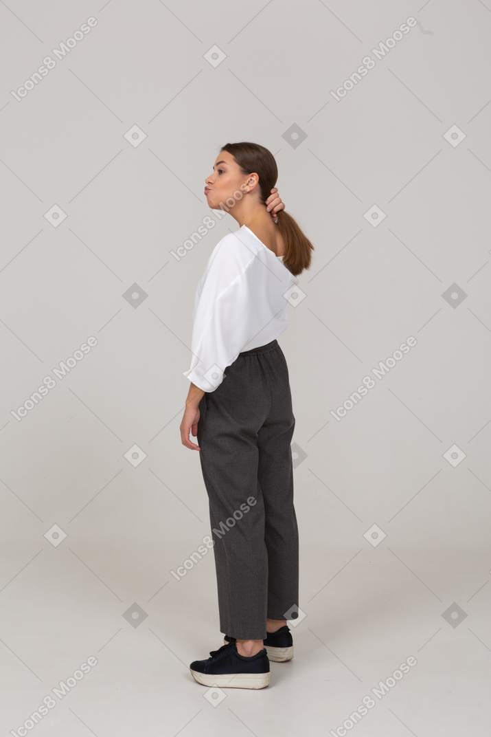 Three-quarter back view of a pouting young lady in office clothing touching her hair