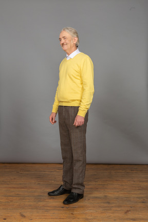 Three-quarter view of an old cheerful man in yellow pullover smiling and looking aside hopefully