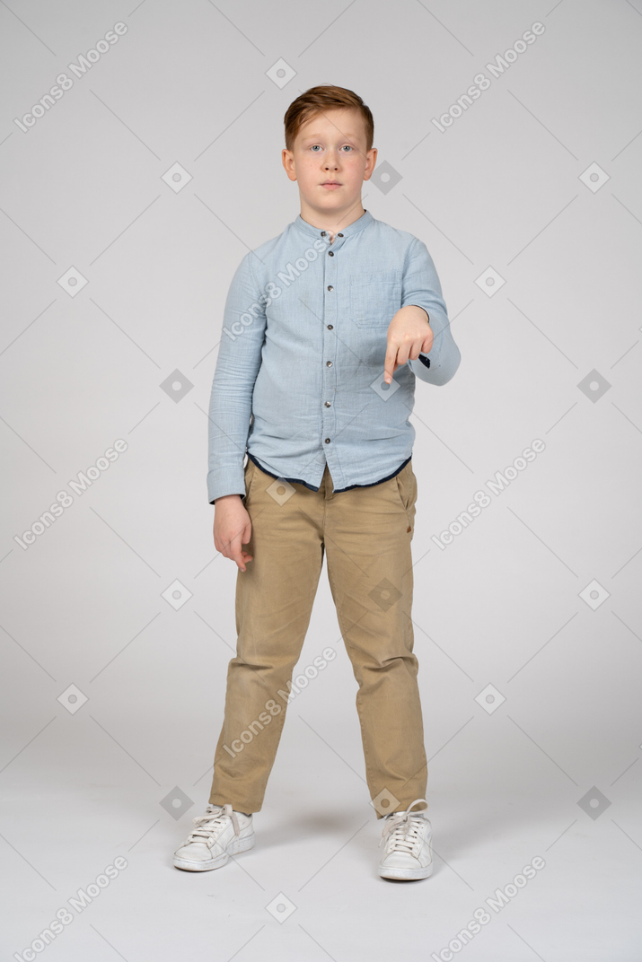 Front view of a boy pointing down with finger and looking at camera