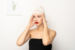 Young woman with bandaged head touching temples