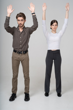Front view of a young couple in office clothing raising hands