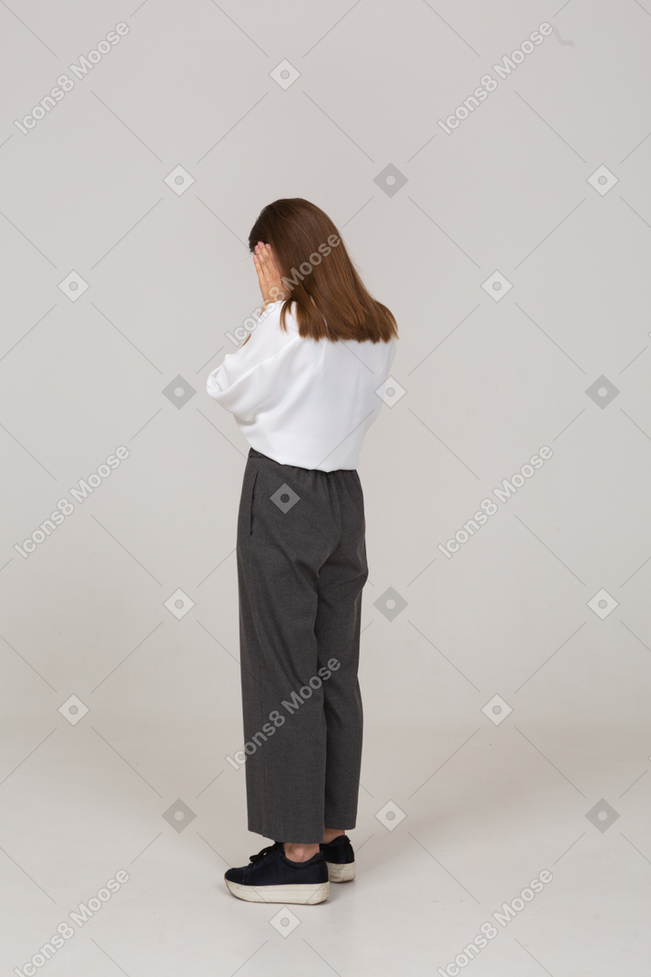 Three-quarter back view of a young lady in office clothing touching ears