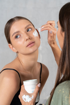 Mujer aplicando crema facial en la cara de otra mujer