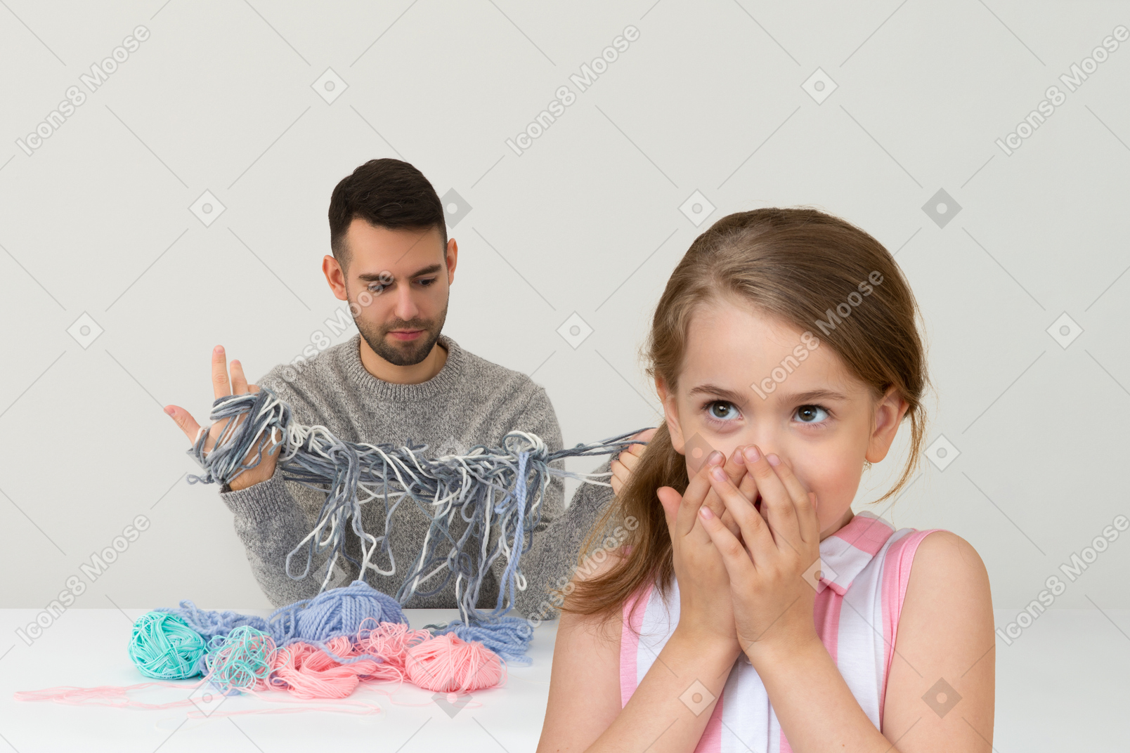 Confused little girl against her father who's looking at tangled mess of yarn