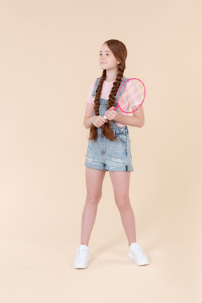 Teenage girl holding tennis racket and standing back to camera