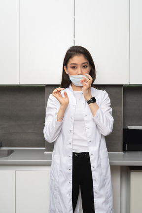 Vista frontal de una doctora ajustando su máscara protectora y mirando a la cámara