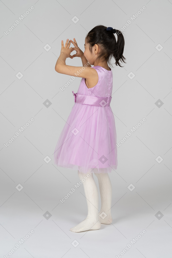 Three-quarter back view of a little girl making a heart with her hands