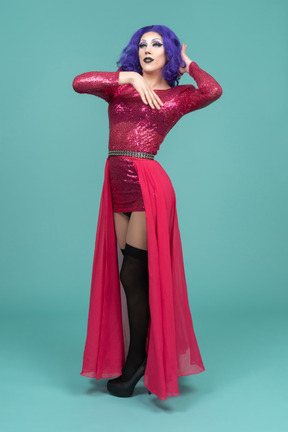 Portrait of a drag queen in pink dress touching their hair & raising arm