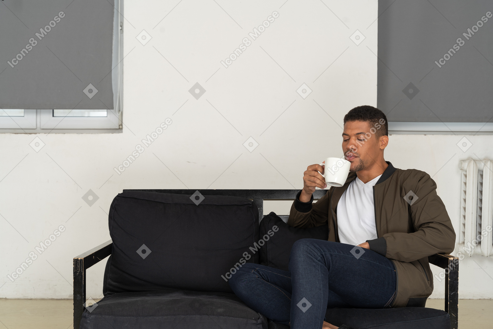 Vista frontal de un joven soñando sentado en un sofá mientras bebe café
