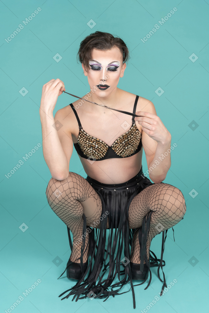 Drag queen squatting with leather stripe in hands