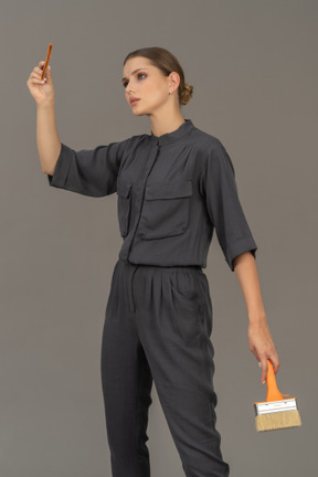 Woman in gray coveralls posing with paint brushes