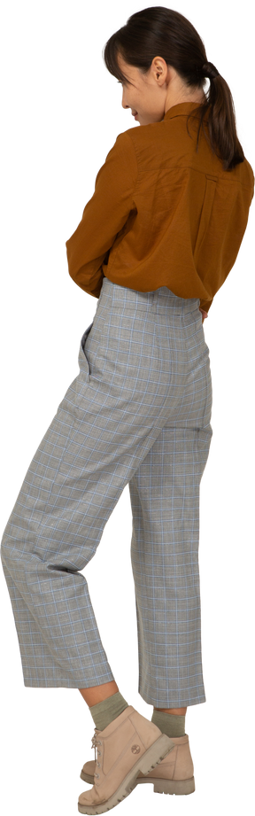 Vista posteriore di tre quarti di una giovane donna asiatica in calzoni e camicetta che incrocia le braccia