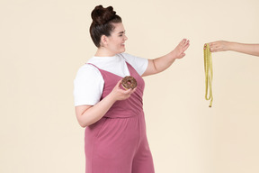 Young plus size woman in a fuchsia jumpsuit posing with food against a pastel yellow background