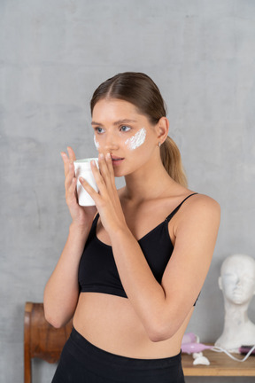 Jeune femme avec de la crème sur les joues regardant de côté