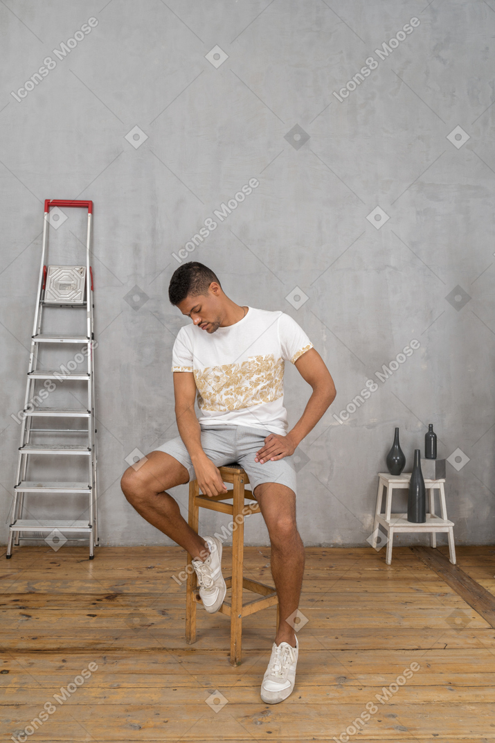 A man sits on a chair in front of a wall of graffiti