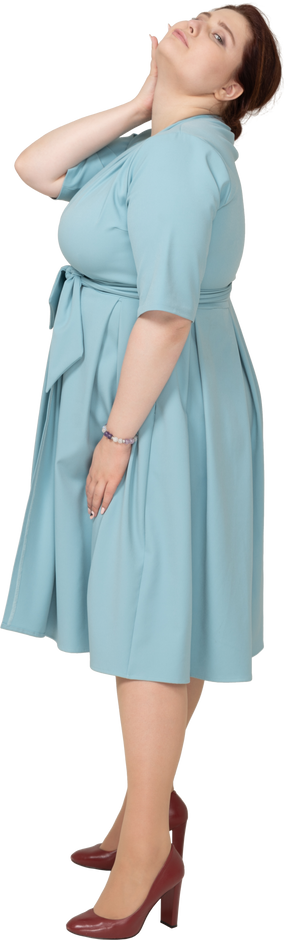 Vista laterale di una donna in abito blu in posa con la mano sul collo