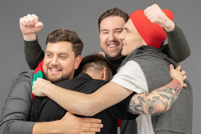 Close-up of four male football fans celebrating the victory & hugging