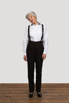 Front view of an old grimacing female in office clothes  touching head to shoulder