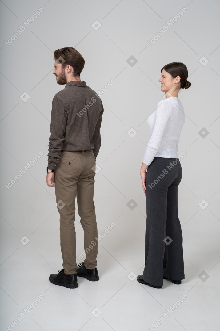 Vista posterior de tres cuartos de una pareja joven disgustada haciendo muecas en ropa de oficina