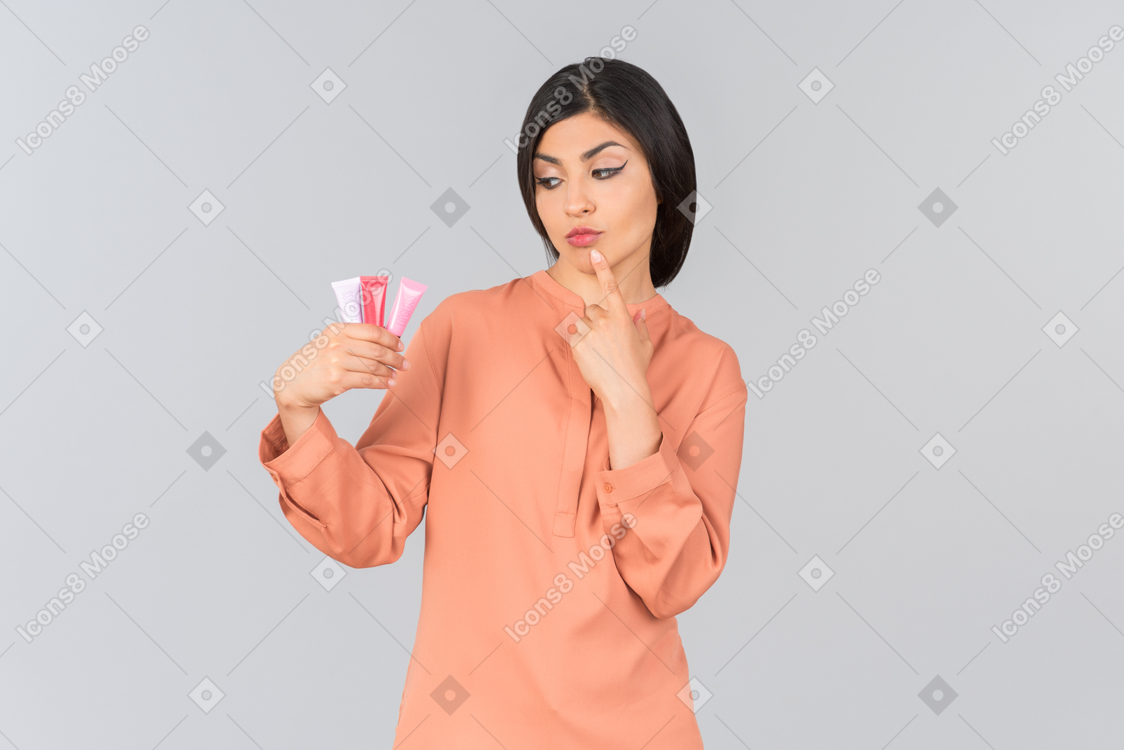 Pensive indian woman choosing from lip balms she's holding
